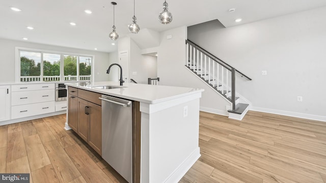 kitchen with appliances with stainless steel finishes, sink, a center island with sink, white cabinets, and hanging light fixtures