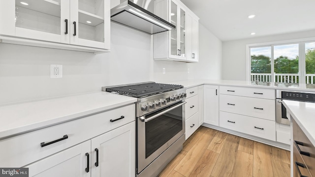 kitchen featuring white cabinets, appliances with stainless steel finishes, light hardwood / wood-style flooring, and wall chimney exhaust hood