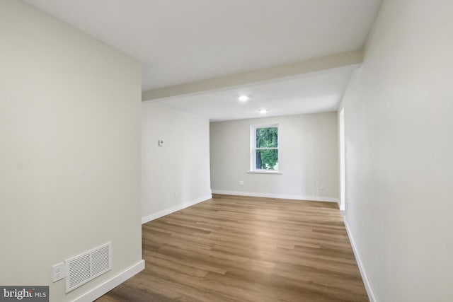 spare room with beamed ceiling and wood-type flooring