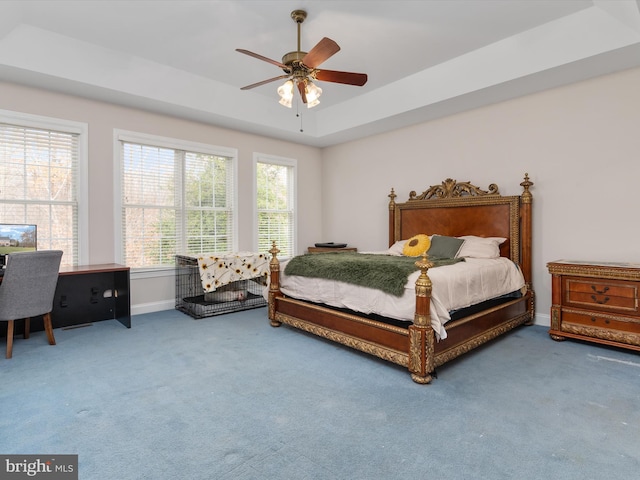 carpeted bedroom with a raised ceiling and ceiling fan