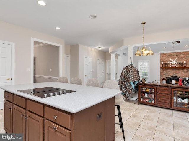 kitchen with a brick fireplace, decorative light fixtures, a kitchen bar, black electric stovetop, and a kitchen island