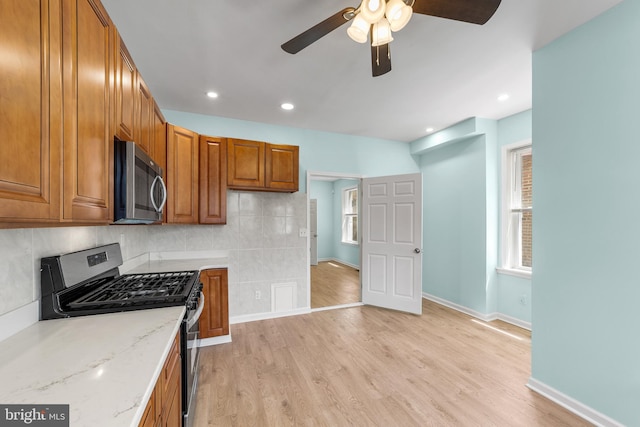 kitchen featuring ceiling fan, appliances with stainless steel finishes, light stone countertops, light hardwood / wood-style floors, and decorative backsplash