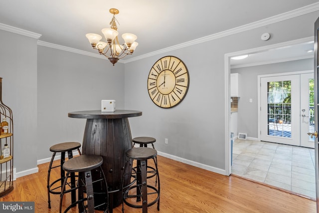 dining space featuring light hardwood / wood-style flooring, ornamental molding, french doors, and an inviting chandelier