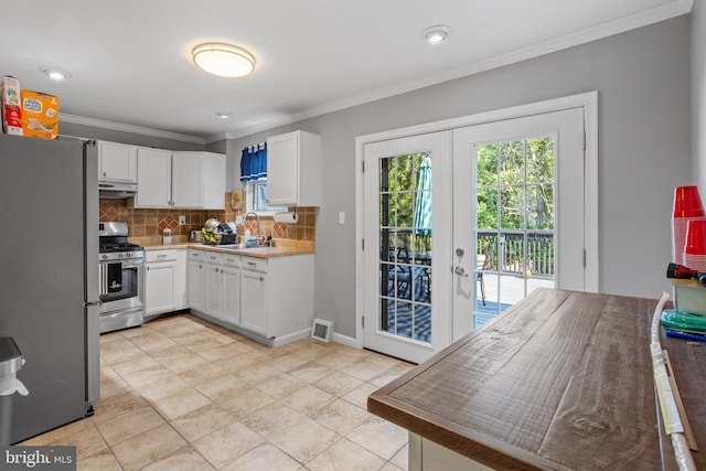 kitchen featuring appliances with stainless steel finishes, white cabinetry, french doors, tasteful backsplash, and ornamental molding