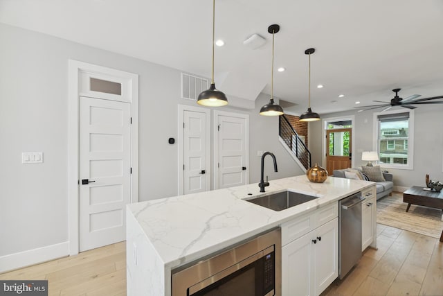 kitchen featuring decorative light fixtures, white cabinetry, stainless steel appliances, sink, and a center island with sink