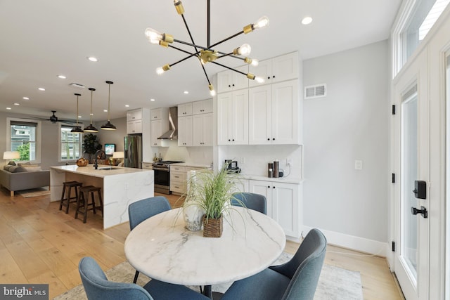 dining room featuring light wood-type flooring, sink, and ceiling fan with notable chandelier