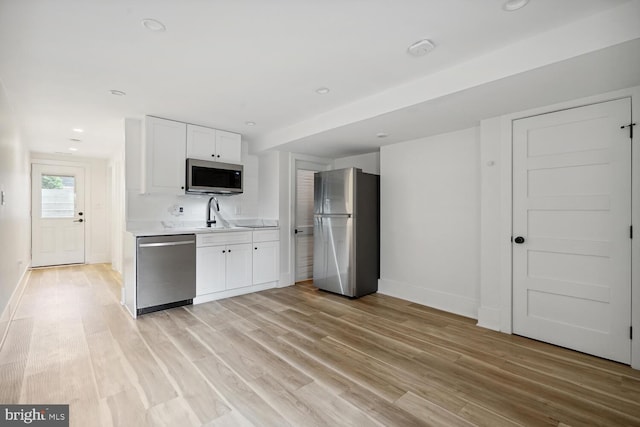 kitchen with appliances with stainless steel finishes, light hardwood / wood-style flooring, white cabinets, and sink