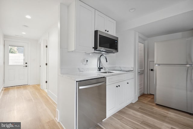 kitchen featuring white cabinets, stainless steel appliances, decorative backsplash, sink, and light hardwood / wood-style flooring