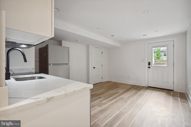 kitchen featuring light hardwood / wood-style floors, fridge, sink, light stone countertops, and white cabinets