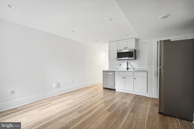 kitchen featuring stainless steel appliances, decorative backsplash, white cabinets, light hardwood / wood-style flooring, and sink