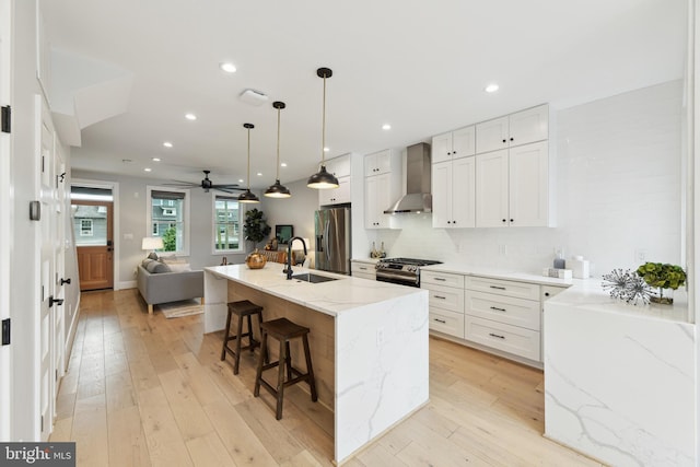 kitchen featuring an island with sink, wall chimney range hood, white cabinetry, and stainless steel appliances