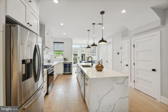 kitchen featuring wine cooler, pendant lighting, white cabinetry, a kitchen island with sink, and appliances with stainless steel finishes