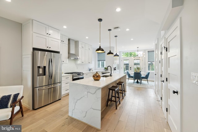 kitchen with white cabinets, wall chimney exhaust hood, stainless steel appliances, sink, and a center island with sink