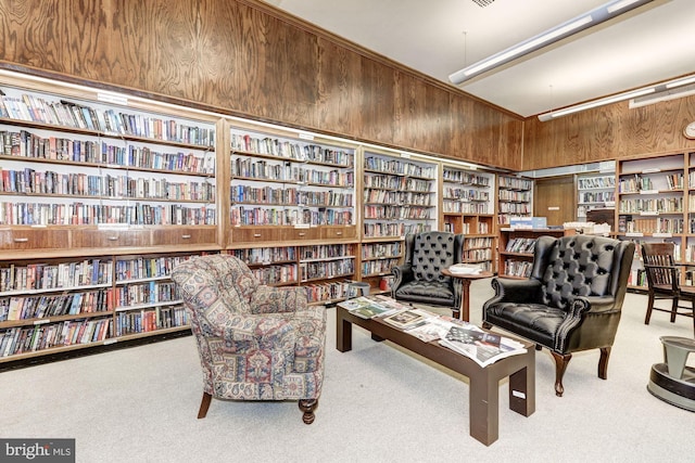 living area featuring a towering ceiling, light colored carpet, built in shelves, and wooden walls