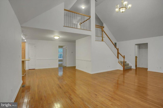 unfurnished living room with light hardwood / wood-style floors, high vaulted ceiling, and a notable chandelier