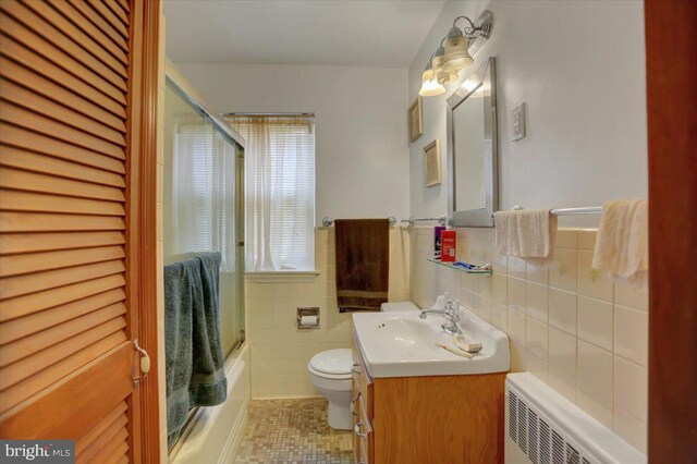 full bathroom with vanity, shower / bath combination with glass door, radiator, tile patterned floors, and tile walls