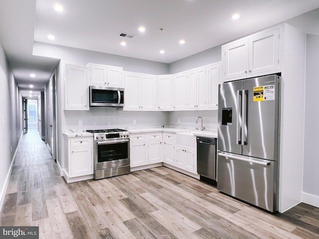 kitchen featuring light stone countertops, premium appliances, sink, light hardwood / wood-style flooring, and white cabinets