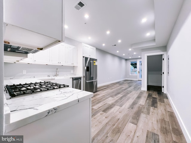 kitchen featuring white cabinets, sink, light hardwood / wood-style flooring, appliances with stainless steel finishes, and light stone counters