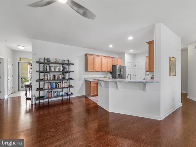 kitchen featuring a kitchen bar, kitchen peninsula, stainless steel fridge, and dark hardwood / wood-style floors