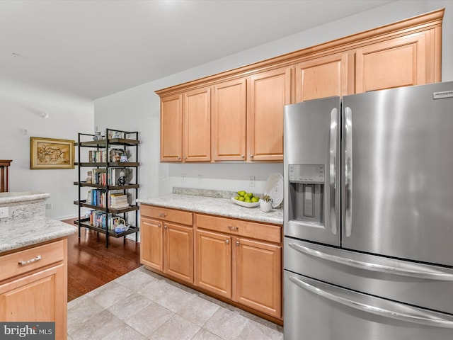 kitchen with light stone counters, stainless steel fridge with ice dispenser, and light tile patterned floors