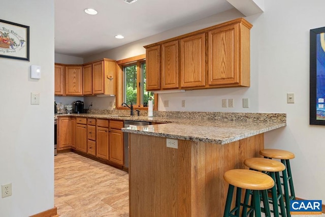 kitchen featuring kitchen peninsula, light stone counters, stainless steel dishwasher, a breakfast bar, and sink