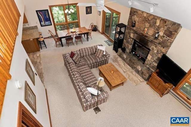 carpeted living room with a fireplace, ceiling fan with notable chandelier, track lighting, and high vaulted ceiling