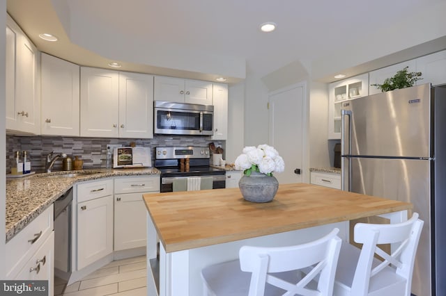 kitchen with decorative backsplash, white cabinetry, stainless steel appliances, and wooden counters