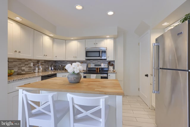 kitchen featuring a breakfast bar, white cabinets, decorative backsplash, butcher block counters, and stainless steel appliances