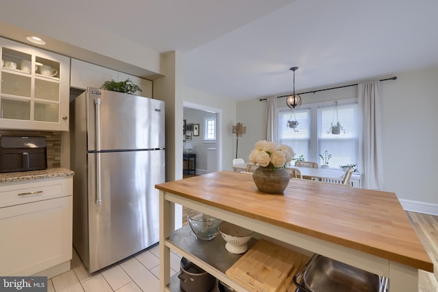 kitchen with white cabinetry, stainless steel fridge, decorative light fixtures, and wood counters