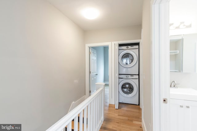 laundry room with sink, stacked washer and dryer, and light hardwood / wood-style floors