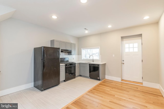 kitchen featuring backsplash, sink, light hardwood / wood-style flooring, gray cabinetry, and black appliances