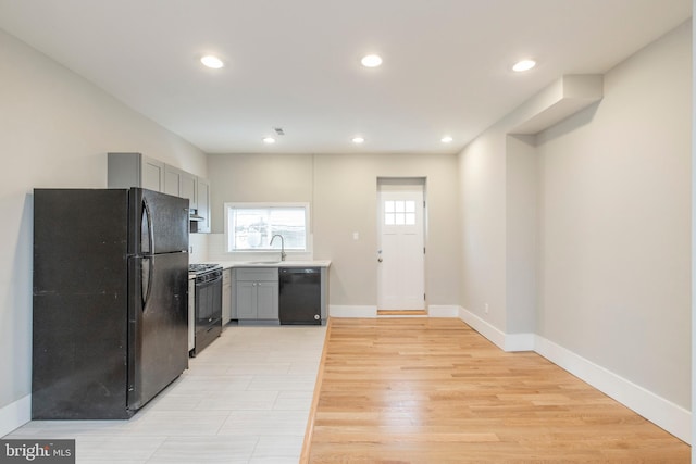 kitchen featuring light hardwood / wood-style floors, tasteful backsplash, sink, black appliances, and gray cabinetry