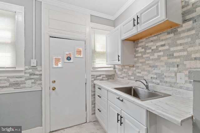 kitchen with backsplash, sink, ornamental molding, light stone counters, and white cabinetry