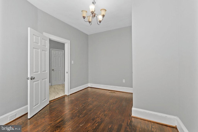 empty room with dark wood-type flooring and an inviting chandelier