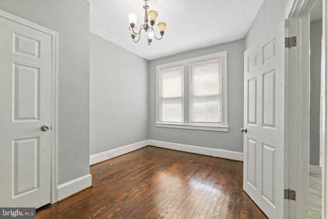 empty room featuring dark hardwood / wood-style flooring and an inviting chandelier