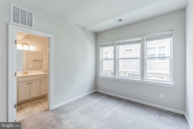 unfurnished bedroom with ensuite bathroom, sink, and light colored carpet