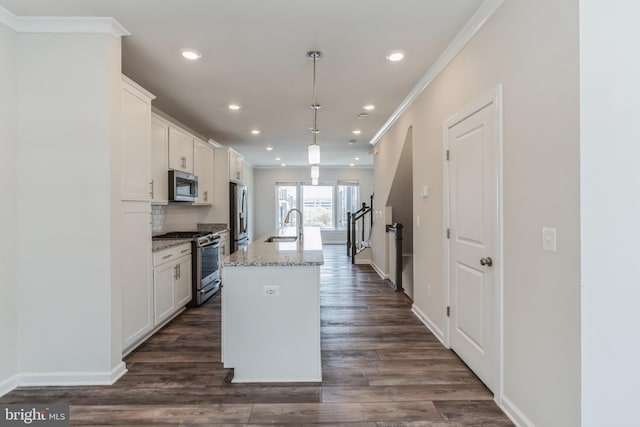 kitchen with appliances with stainless steel finishes, light stone counters, an island with sink, white cabinets, and decorative light fixtures