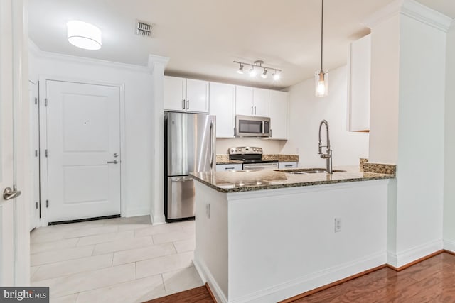 kitchen featuring dark stone countertops, rail lighting, stainless steel appliances, pendant lighting, and sink