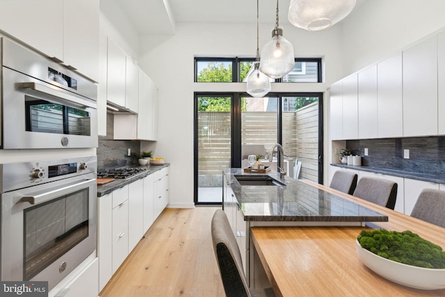 kitchen with a sink, light wood-style floors, pendant lighting, white cabinetry, and tasteful backsplash