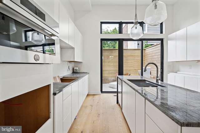 kitchen with pendant lighting, light hardwood / wood-style flooring, sink, and white cabinets