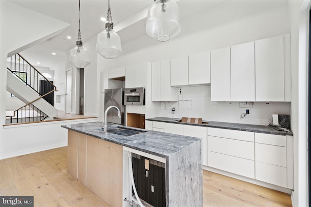 kitchen with an island with sink, light hardwood / wood-style flooring, sink, and white cabinets