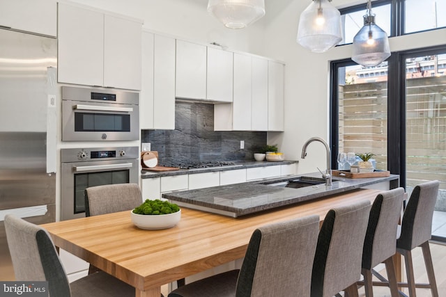 kitchen with sink, white cabinetry, appliances with stainless steel finishes, pendant lighting, and backsplash