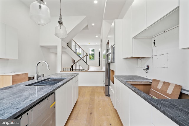 kitchen with dark stone countertops, white cabinetry, light hardwood / wood-style flooring, and sink