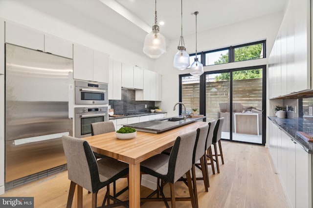 kitchen with tasteful backsplash, white cabinetry, sink, hanging light fixtures, and stainless steel appliances