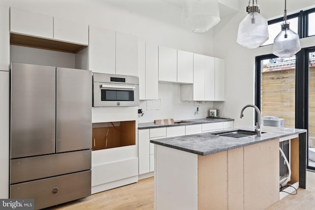 kitchen featuring oven, light hardwood / wood-style flooring, decorative light fixtures, stainless steel fridge, and a kitchen island with sink