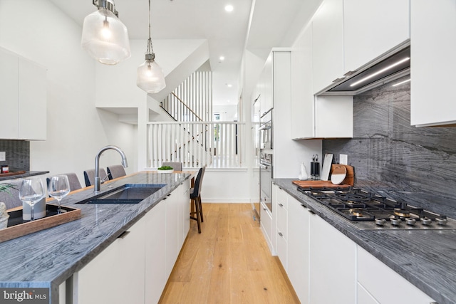 kitchen featuring stainless steel appliances, white cabinetry, pendant lighting, and wall chimney range hood