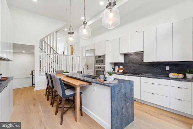 kitchen with sink, a kitchen island with sink, light hardwood / wood-style floors, white cabinets, and decorative light fixtures