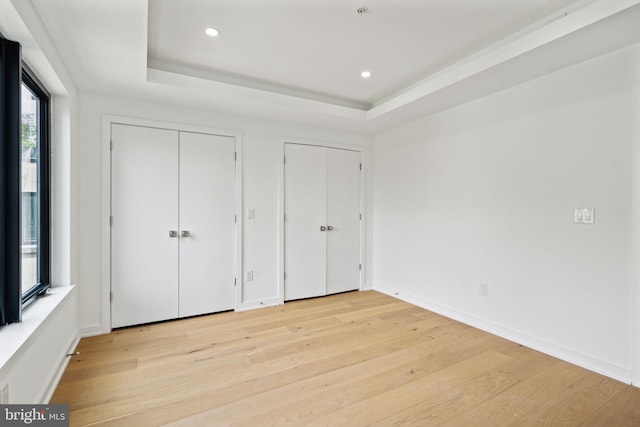 unfurnished bedroom featuring light wood-type flooring, a raised ceiling, and two closets