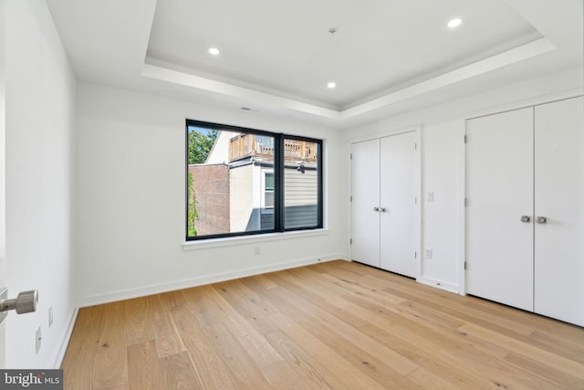 unfurnished bedroom with a tray ceiling, light hardwood / wood-style floors, and two closets