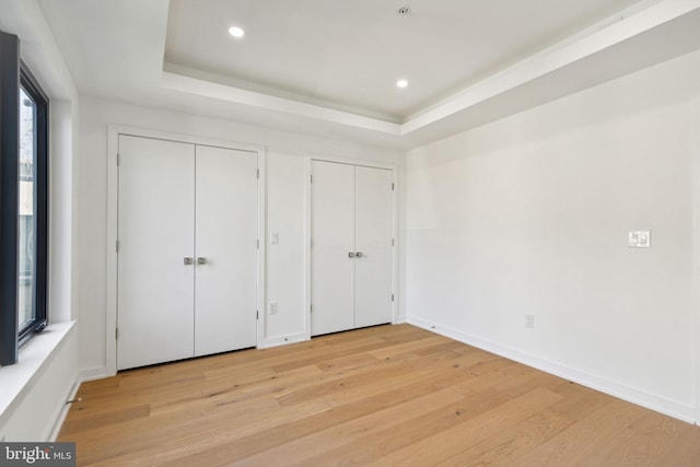 unfurnished bedroom featuring a tray ceiling, light hardwood / wood-style flooring, and two closets